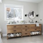 wide view of dual sink vanity beneath window and round mirror